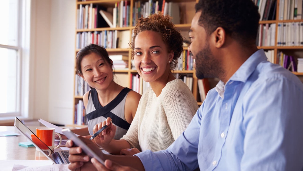 Three people chatting in a bright office.
