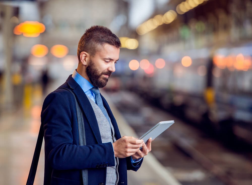 Un homme d’âge moyen regarde une tablette dans une gare.